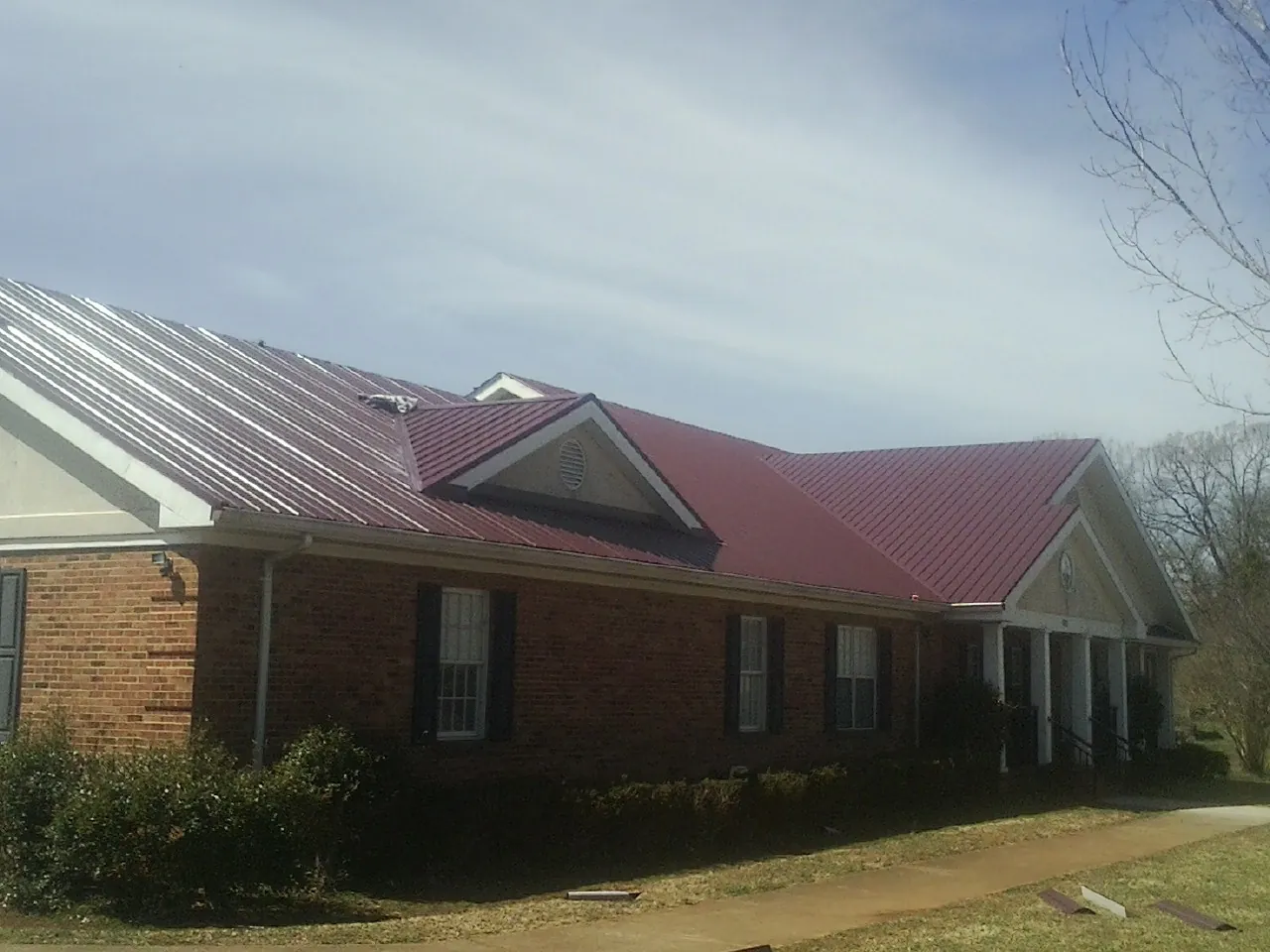Red metal roof with gabled entries on a long brick building, from a Hail Damage Roof Repair job in Mira Loma