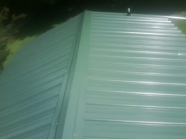 New green metal panels meeting at the ridge of a roof — Flat Roof Repair work by our crew in Mira Loma