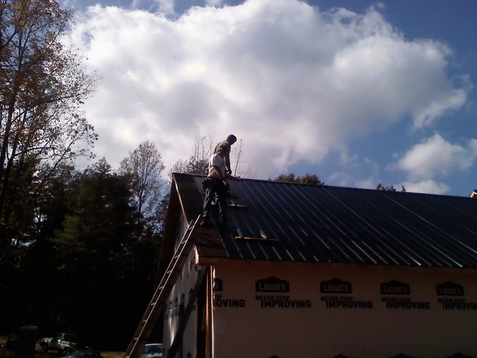 Roofer fastening dark metal panels high against a cloudy sky, from a Roof Inspection job in Mira Loma