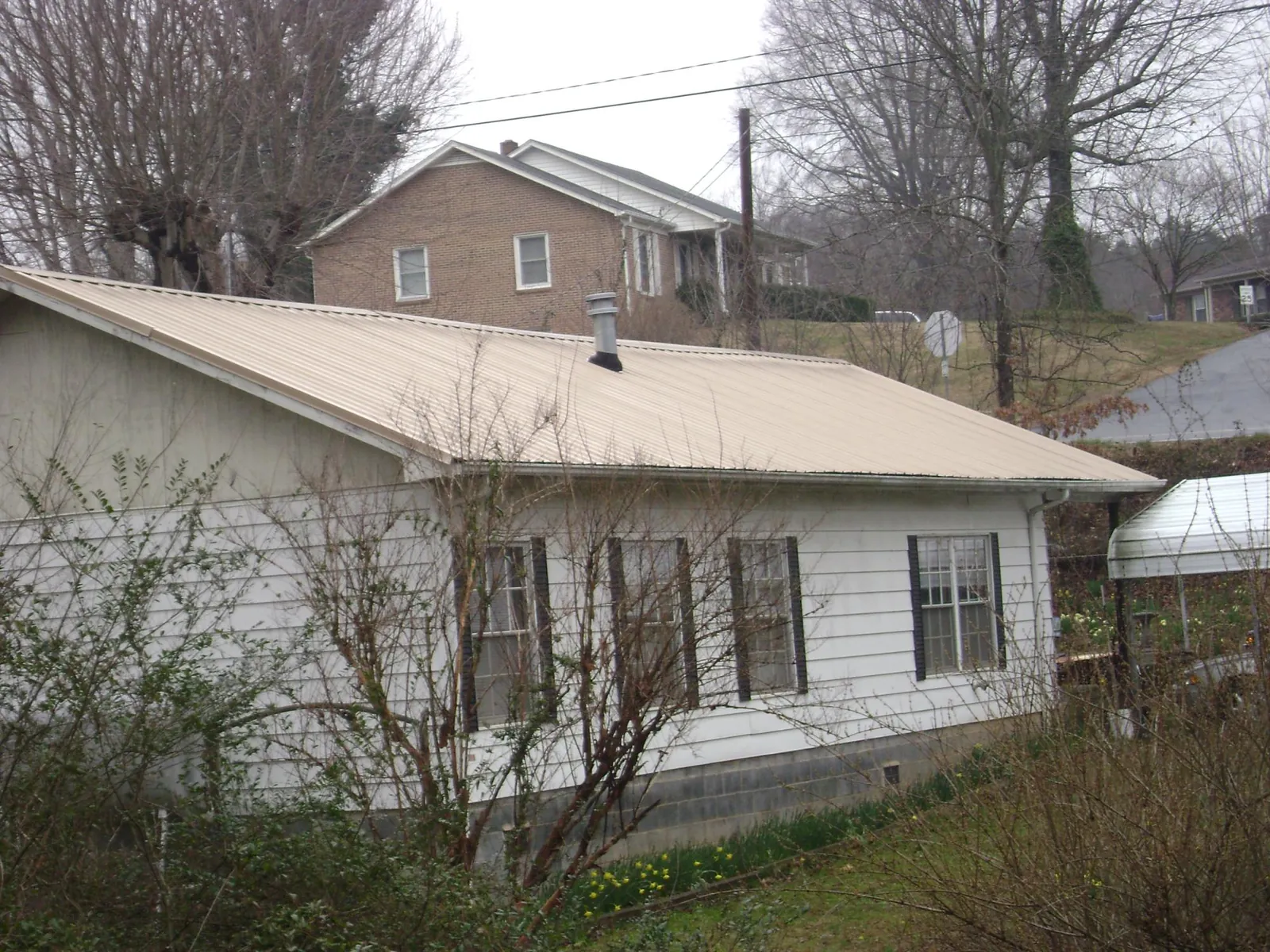 Tan metal roof on a white sided house set into a hillside — Commercial Roofing by Roofing Brothers in Mira Loma